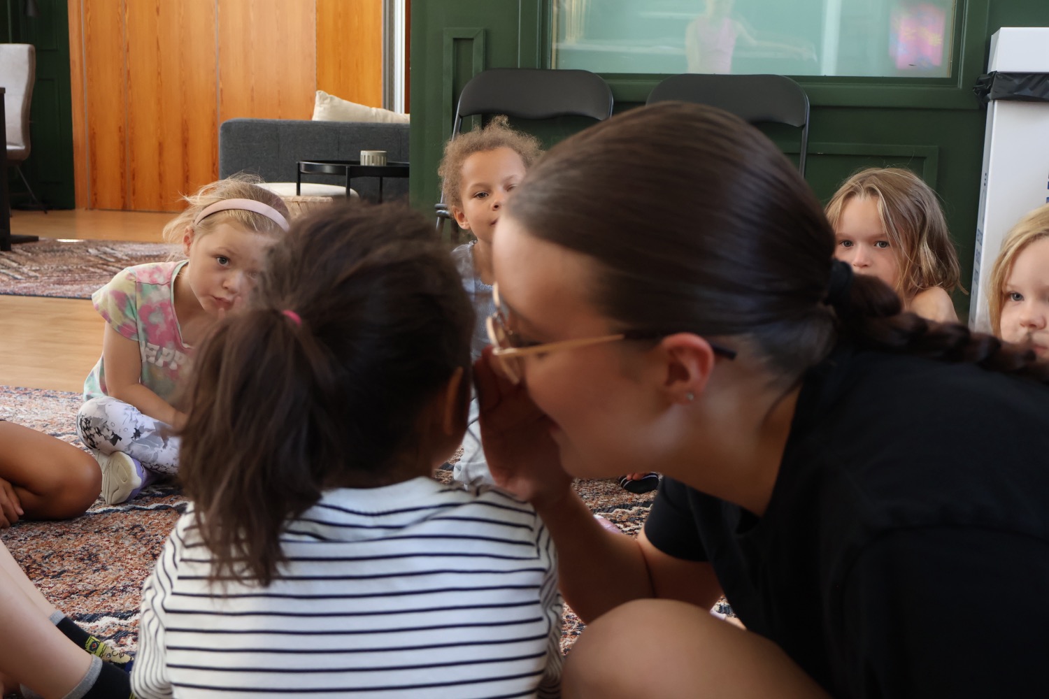 Pedagog sitter på golvet och pratar nära med barnen i en samlingsstund