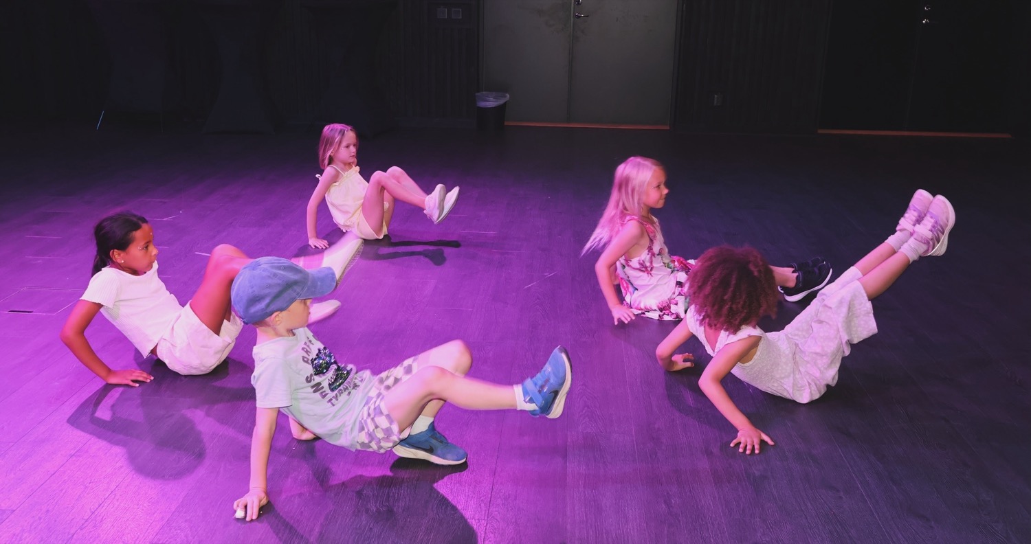 Fem barn i en lekfull golvpose i dansstudion i lila scenljus