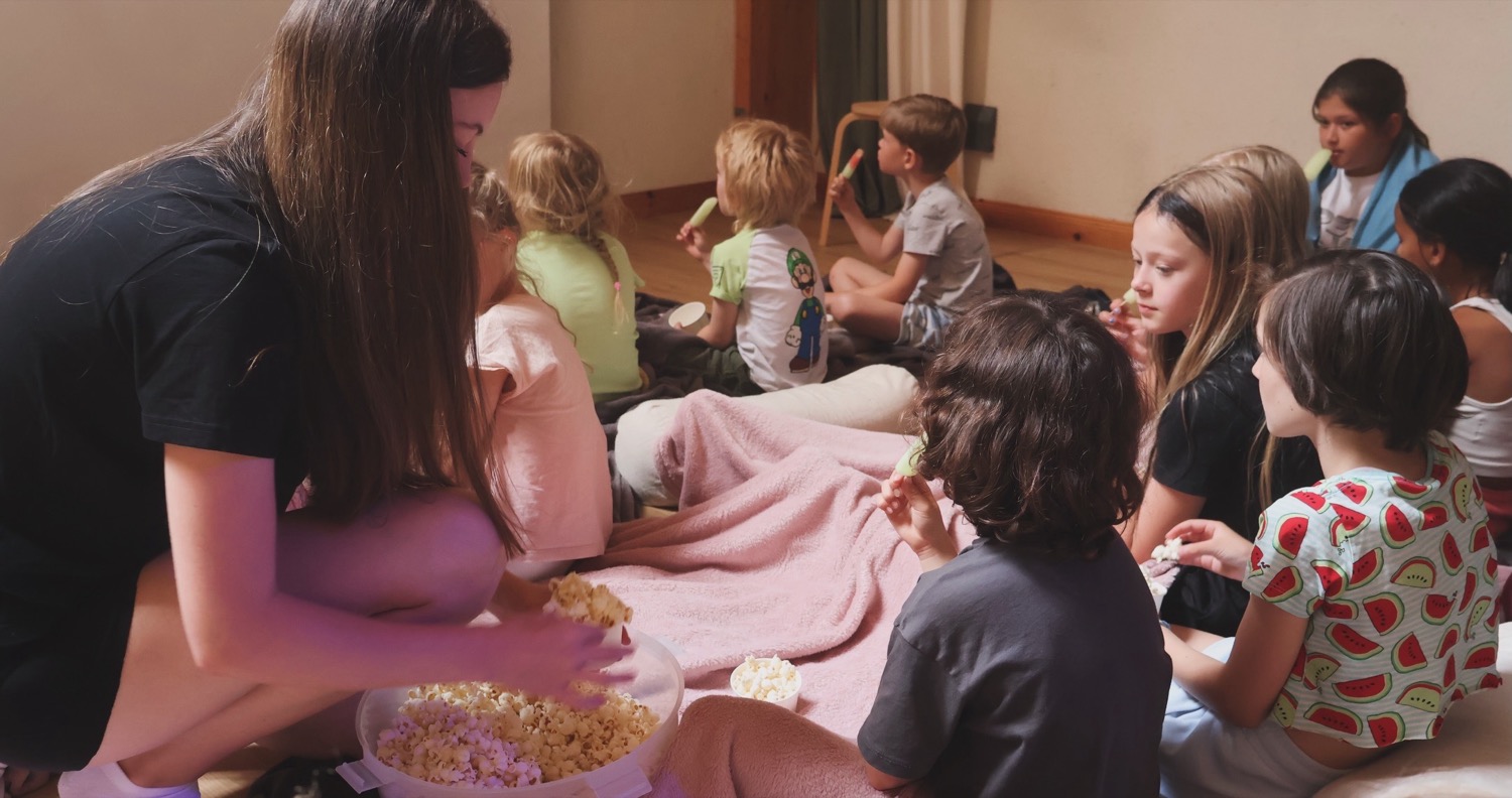 Pedagog delar ut popcorn till barnen under en mysstund på lägret