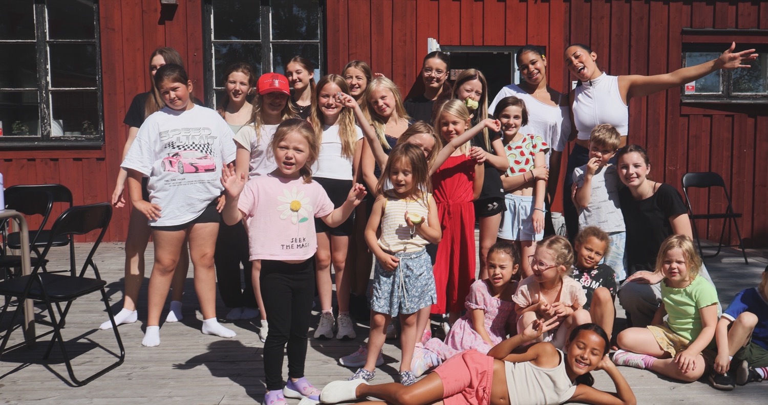 Hela läger-gänget samlas för en gruppbild framför den röda stugan i solen